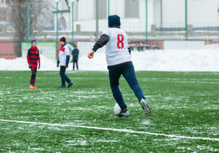 Młodzi zawodnicy wykonujący slalom z piłką między pachołkami zimą